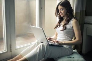 Frau sitzt mit Laptop am Fenster