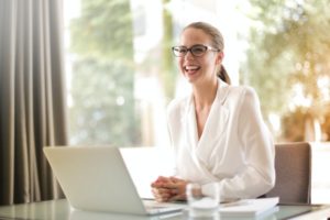 Frau lacht sitzend am weißen Laptop